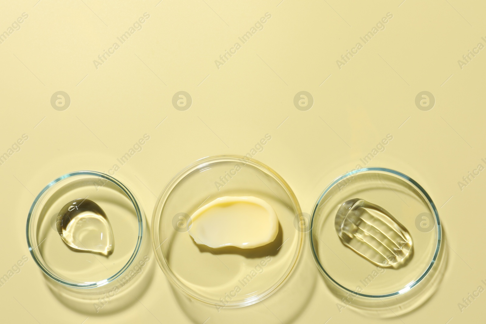 Different cosmetic products in Petri dishes on pale yellow background, flat lay. Space for text Photo of Different cosmetic products in Petri dishes on pale yellow background, flat lay. Space for text