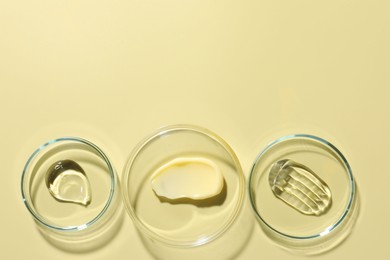 Photo of Different cosmetic products in Petri dishes on pale yellow background, flat lay. Space for text