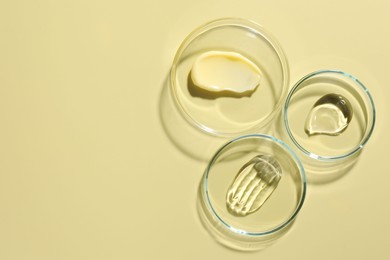 Photo of Different cosmetic products in Petri dishes on pale yellow background, flat lay. Space for text