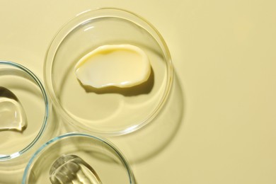 Photo of Different cosmetic products in Petri dishes on pale yellow background, flat lay. Space for text