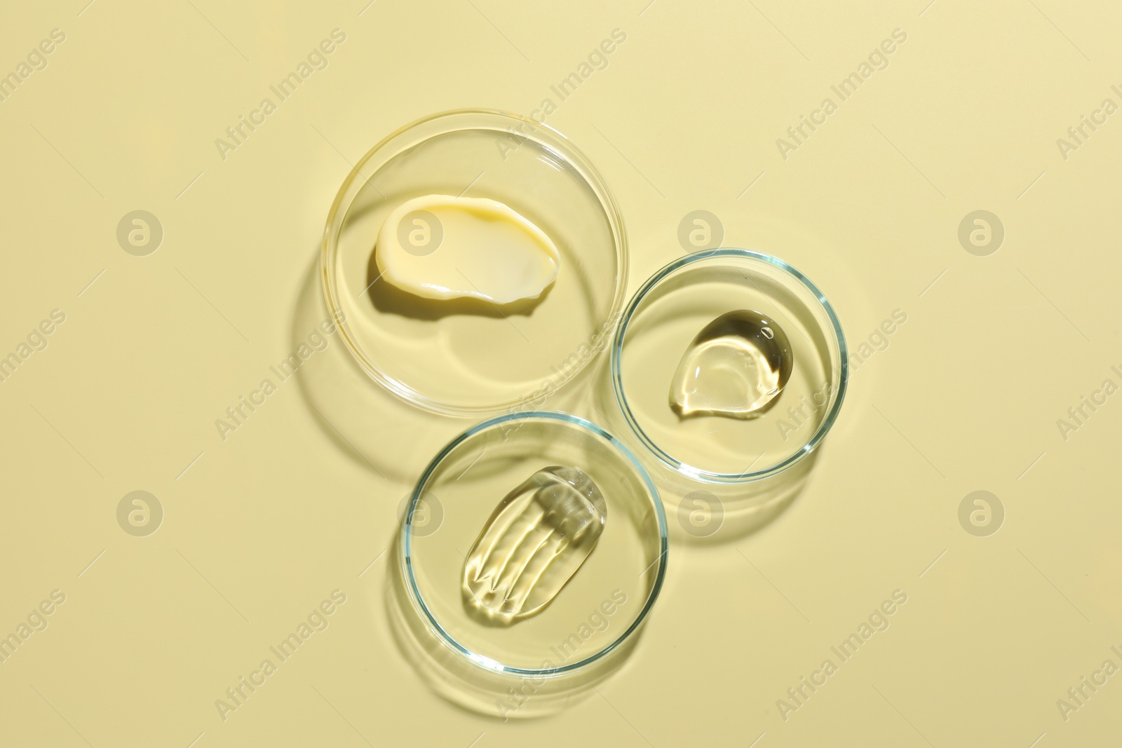 Different cosmetic products in Petri dishes on pale yellow background, flat lay Photo of Different cosmetic products in Petri dishes on pale yellow background, flat lay