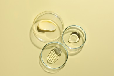 Photo of Different cosmetic products in Petri dishes on pale yellow background, flat lay
