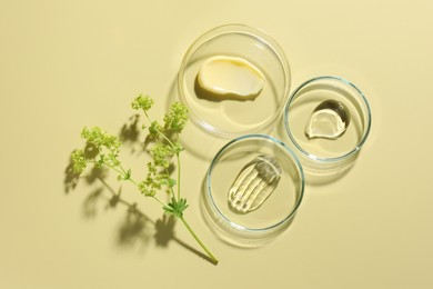 Photo of Different cosmetic products in Petri dishes and floral decor on pale yellow background, flat lay