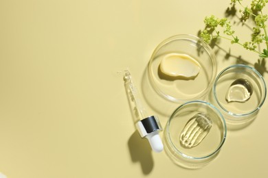 Photo of Different cosmetic products in Petri dishes, dropper and floral decor on pale yellow background, flat lay. Space for text
