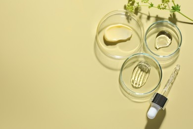 Photo of Different cosmetic products in Petri dishes, dropper and floral decor on pale yellow background, flat lay. Space for text
