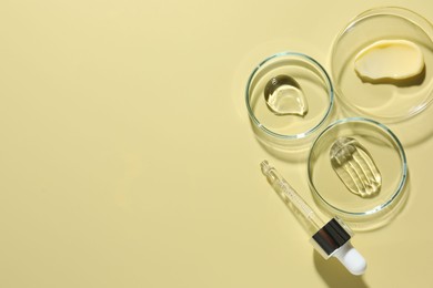 Photo of Different cosmetic products in Petri dishes and dropper on pale yellow background, flat lay. Space for text