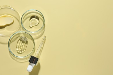 Photo of Different cosmetic products in Petri dishes and dropper on pale yellow background, flat lay. Space for text