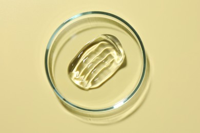 Photo of Cosmetic product in Petri dish on pale yellow background, top view