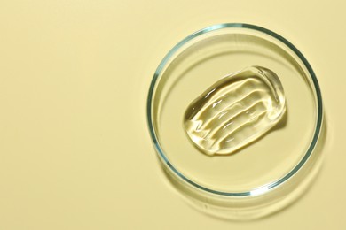 Photo of Cosmetic product in Petri dish on pale yellow background, top view. Space for text
