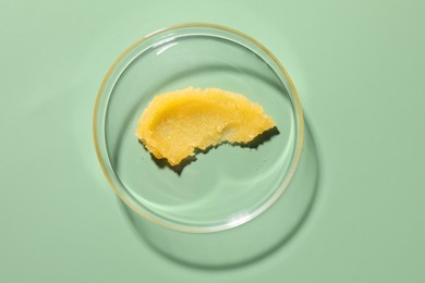 Photo of Cosmetic product in Petri dish on green background, top view