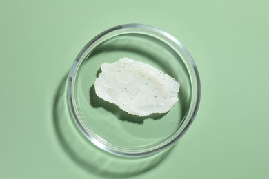 Photo of Cosmetic product in Petri dish on green background, top view