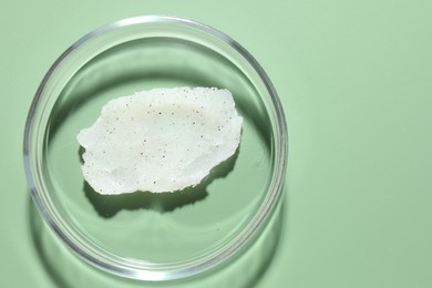 Photo of Cosmetic product in Petri dish on green background, top view. Space for text