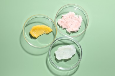 Photo of Different cosmetic products in Petri dishes on green background, flat lay