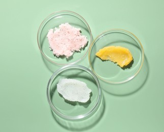 Photo of Different cosmetic products in Petri dishes on green background, flat lay