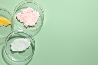 Photo of Different cosmetic products in Petri dishes on green background, flat lay. Space for text