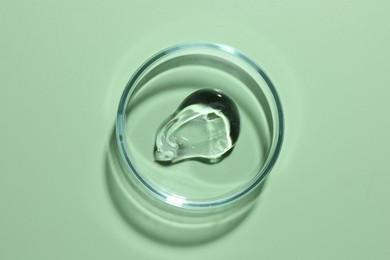Photo of Cosmetic product in Petri dish on green background, top view