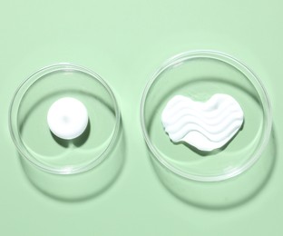 Photo of Different cosmetic products in Petri dishes on green background, flat lay