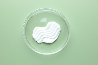 Photo of Cosmetic product in Petri dish on green background, top view
