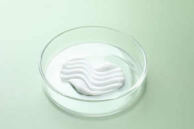 Photo of Cosmetic product in Petri dish on green background, closeup