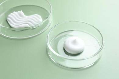 Photo of Different cosmetic products in Petri dishes on green background, closeup