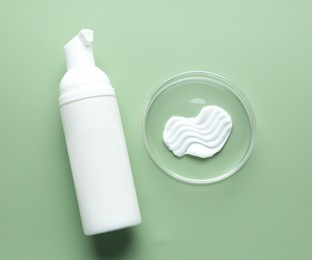 Photo of Cosmetic product in Petri dish and bottle on green background, flat lay