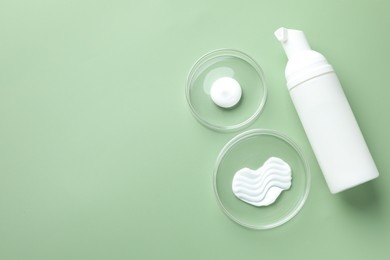 Photo of Different cosmetic products in Petri dishes and bottle on green background, flat lay. Space for text