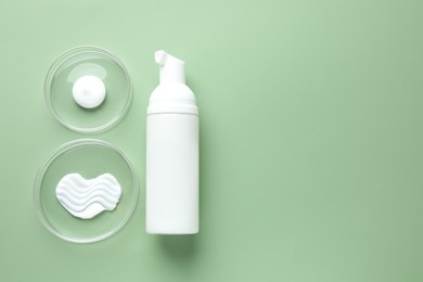 Photo of Different cosmetic products in Petri dishes and bottle on green background, flat lay. Space for text