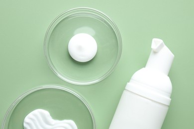 Photo of Different cosmetic products in Petri dishes and bottle on green background, flat lay