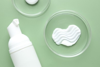 Photo of Different cosmetic products in Petri dishes and bottle on green background, flat lay