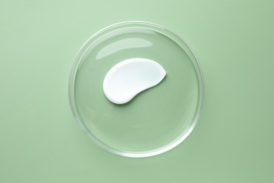 Photo of Cosmetic product in Petri dish on green background, top view