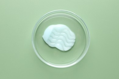 Photo of Cosmetic product in Petri dish on green background, top view
