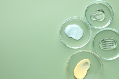 Photo of Different cosmetic products in Petri dishes on green background, flat lay. Space for text