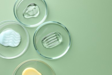 Photo of Different cosmetic products in Petri dishes on green background, flat lay. Space for text