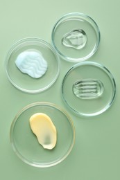 Photo of Different cosmetic products in Petri dishes on green background, flat lay