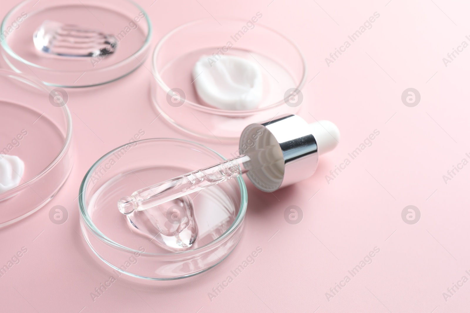 Different cosmetic products in Petri dishes and dropper on pink background, closeup. Space for text Photo of Different cosmetic products in Petri dishes and dropper on pink background, closeup. Space for text