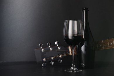 Photo of Acoustic guitar and red wine on black table, closeup. Space for text