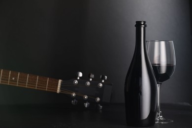 Photo of Acoustic guitar and red wine on black table. Space for text