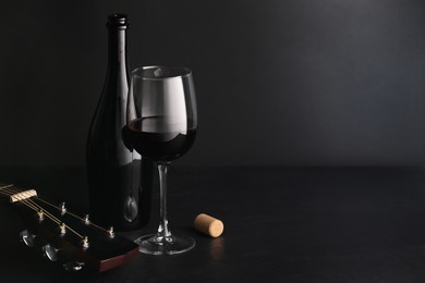 Photo of Acoustic guitar and red wine on black table. Space for text