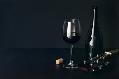 Photo of Acoustic guitar and red wine on black table. Space for text