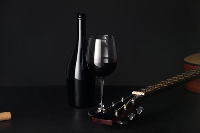 Photo of Acoustic guitar and red wine on black table, closeup