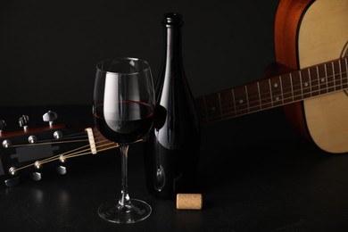Photo of Acoustic guitar and red wine on black table, closeup