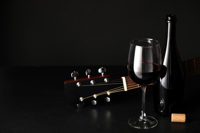 Photo of Acoustic guitar and red wine on black table, closeup. Space for text