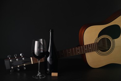 Photo of Acoustic guitar and red wine on black table, closeup. Space for text