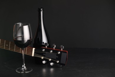 Photo of Acoustic guitar and red wine on black table, closeup. Space for text