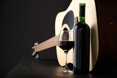 Photo of Acoustic guitar and red wine on black table, closeup