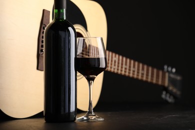 Photo of Acoustic guitar and red wine on black table, closeup
