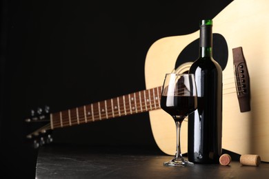Photo of Acoustic guitar and red wine on black table, closeup