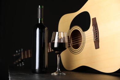 Photo of Acoustic guitar and red wine on black table, closeup