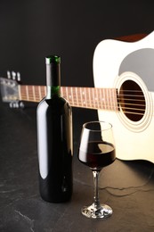 Photo of Acoustic guitar and red wine on black table, closeup