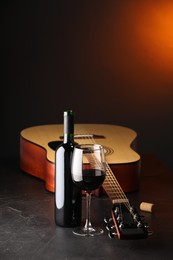 Photo of Acoustic guitar and red wine on black table with brown light, closeup. Space for text